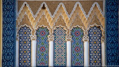 Five narrow ornamental arches with white columns, multicolored zellij, carved stucco, and blue patterned borders at the Royal Palace of Fes.