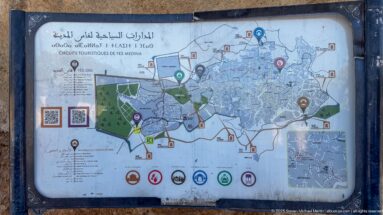 Public tourist map of Fes Medina with colored walking routes, landmark symbols, numbered sites, legend, and QR codes.