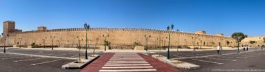 Long ochre crenellated wall in Fes beside a broad roadway and parking area under a clear blue sky.