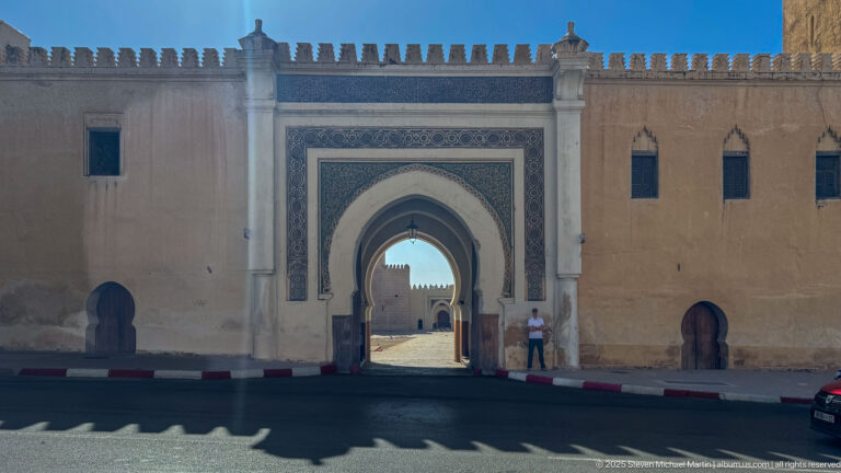 Large pointed gateway in an ochre crenellated wall, framed with geometric ornament and flanked by smaller arched openings.