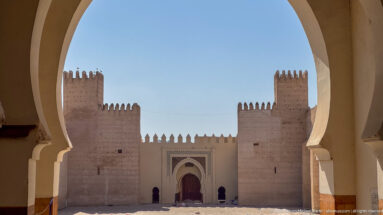 Symmetrical fortified gateway with twin towers and central decorated door, tightly framed by a large foreground arch.
