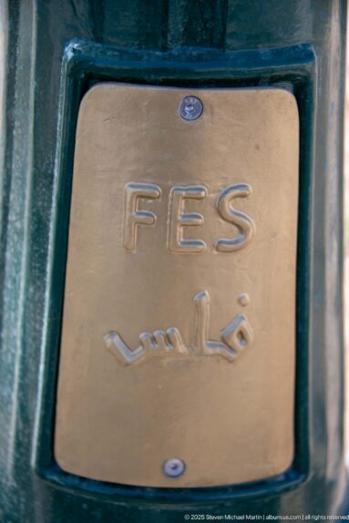 Plaque reading FES above the Arabic name فاس, mounted inside a dark green frame.