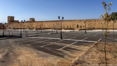 Wide view across an empty paved area toward a long crenellated wall with square towers in Fes.
