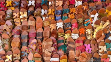 Large market display densely packed with colorful leather sandals in many styles, textures, and strap patterns.