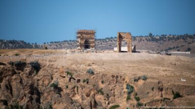 Two standing masonry ruins on a dry hillside near Fes, one enclosed in scaffolding, above a deeply eroded slope.