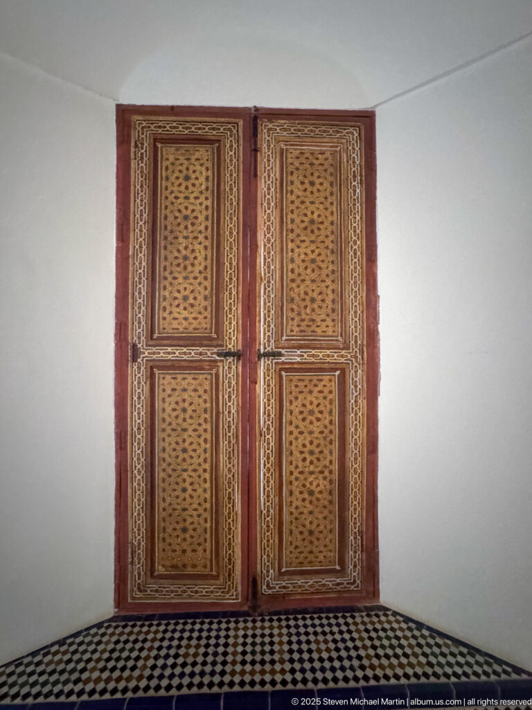 Closed four-panel wooden window with carved geometric perforations above a black-and-white patterned tile floor.