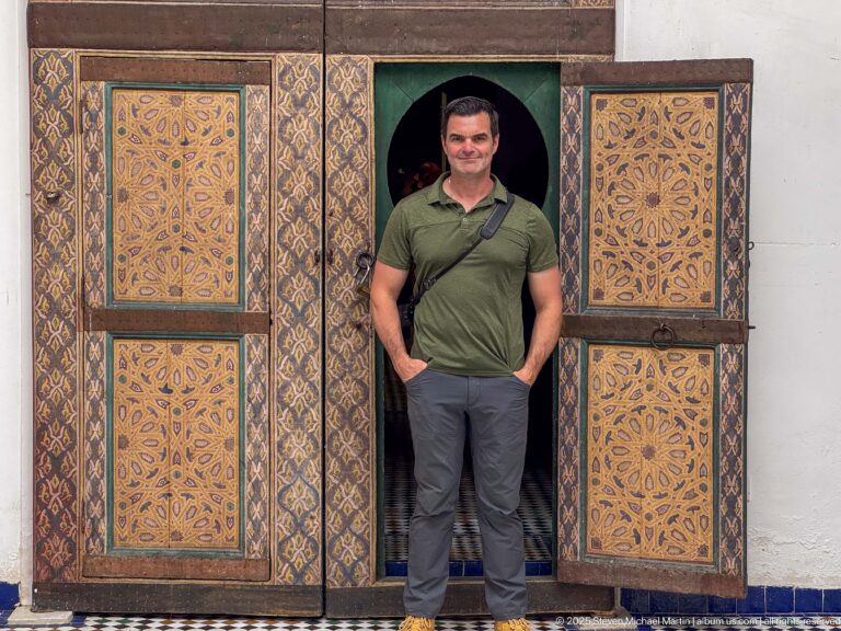 Nineteenth-century decorated wooden main door to Al Batha Palace’s throne hall, with a visitor standing in its small central opening.