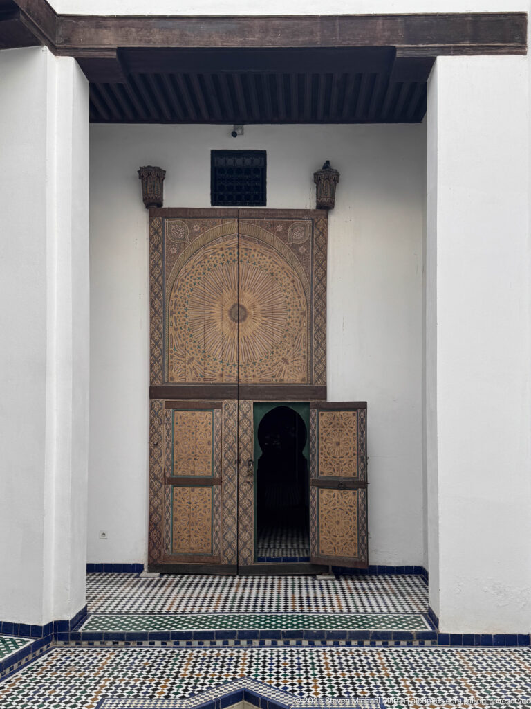 Nineteenth-century decorated wooden main door to Al Batha Palace’s throne hall, seen from across the zellij-paved courtyard.