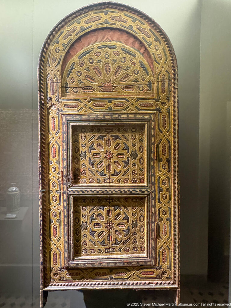 Arched painted wooden cabinet with two calligraphic door panels, radiating ornament above, and multicolored geometric borders.