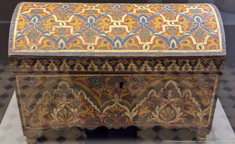Small domed wooden chest painted with red, blue, gold, and green floral ornament, central lock, patterned band, and scalloped feet.