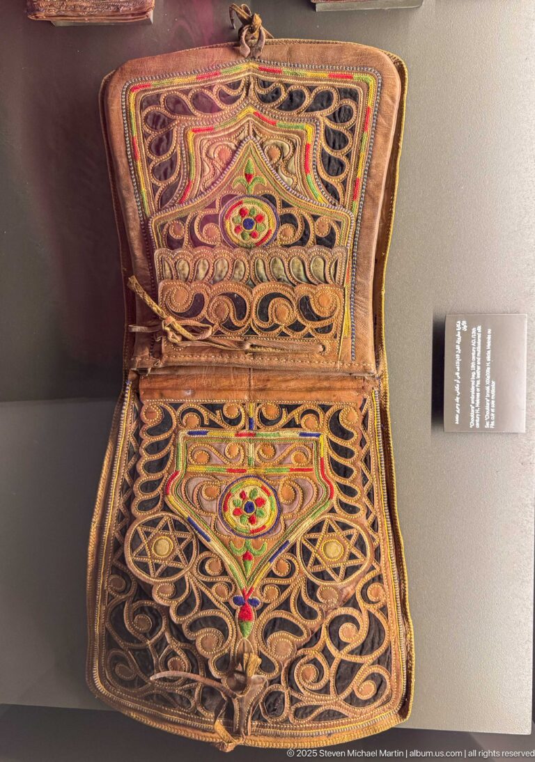 Open folding case with two matching panels of dark looping cord, red and green medallions, and multicolored embroidered decoration.