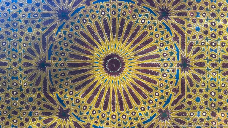 Close-up of blue, yellow, green, white, and purple zellij forming large radiating starbursts with smaller stars and polygons.