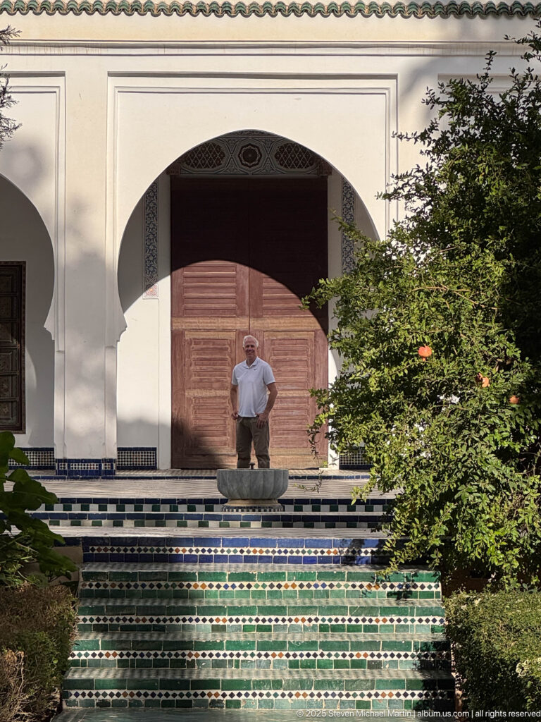 Tiled fountain and steps lead toward a large wooden doorway framed by a white arch, with a visitor standing above.