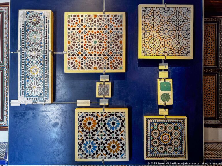 Museum display of multiple zellij panels, including square star patterns, circular rosettes, and smaller geometric samples on a blue wall.