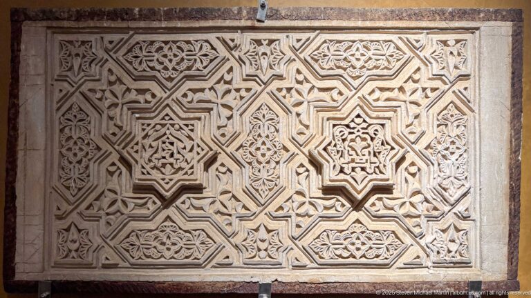 Pale carved relief panel filled with interlocking geometric bands, small rosettes, vegetal motifs, and repeated angular compartments.