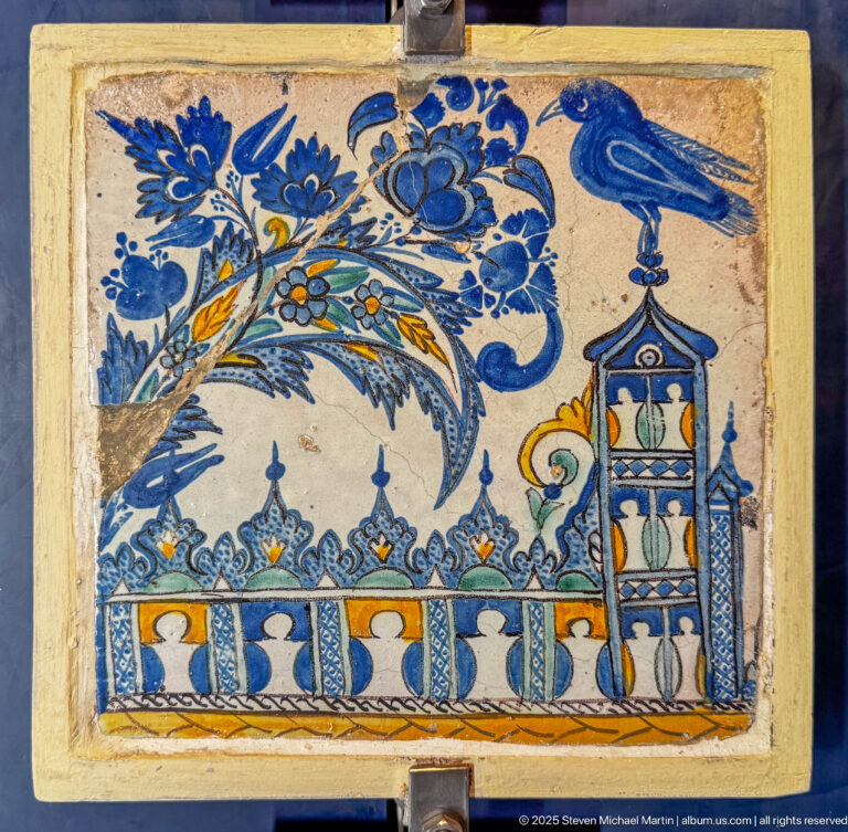 Painted ceramic panel with a large blue bird, flowering branches, and a stylized architectural motif in blue, yellow, green, and orange.