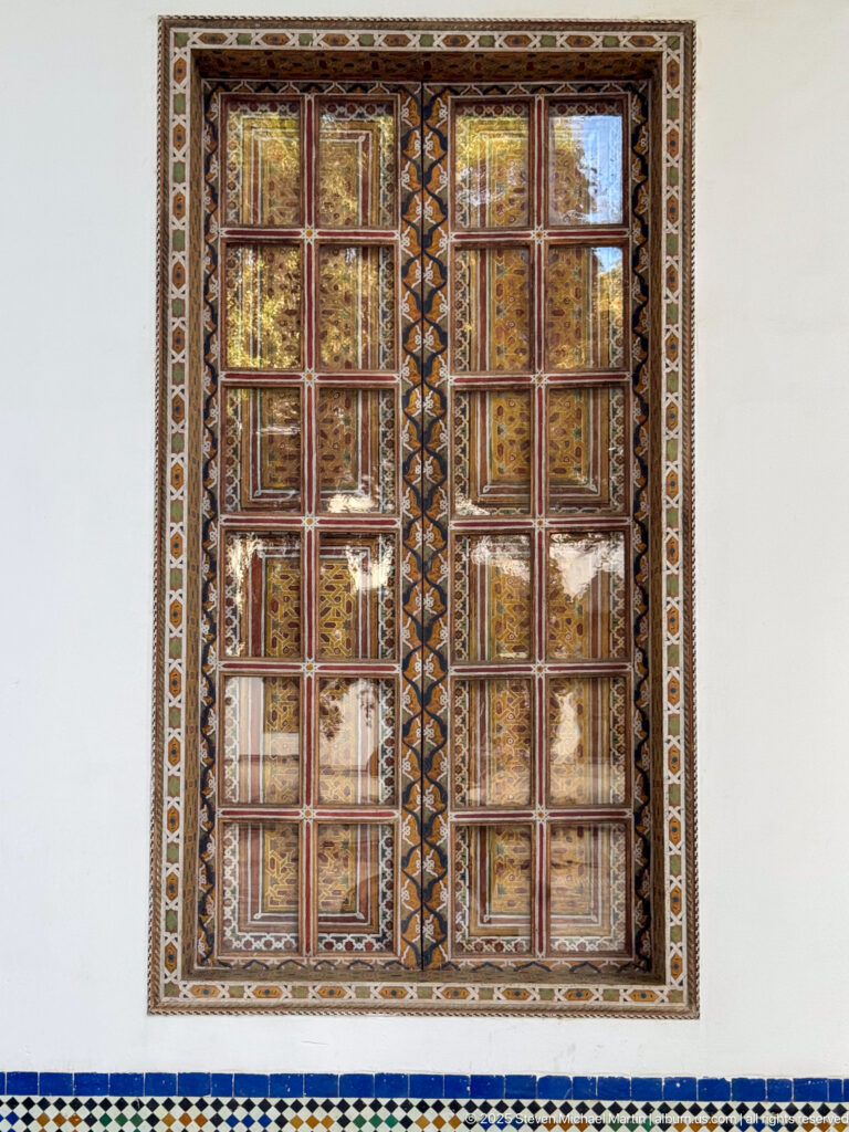 Pair of tall painted wooden shutters with stacked decorative panels, geometric borders, and blue-and-white tilework below.