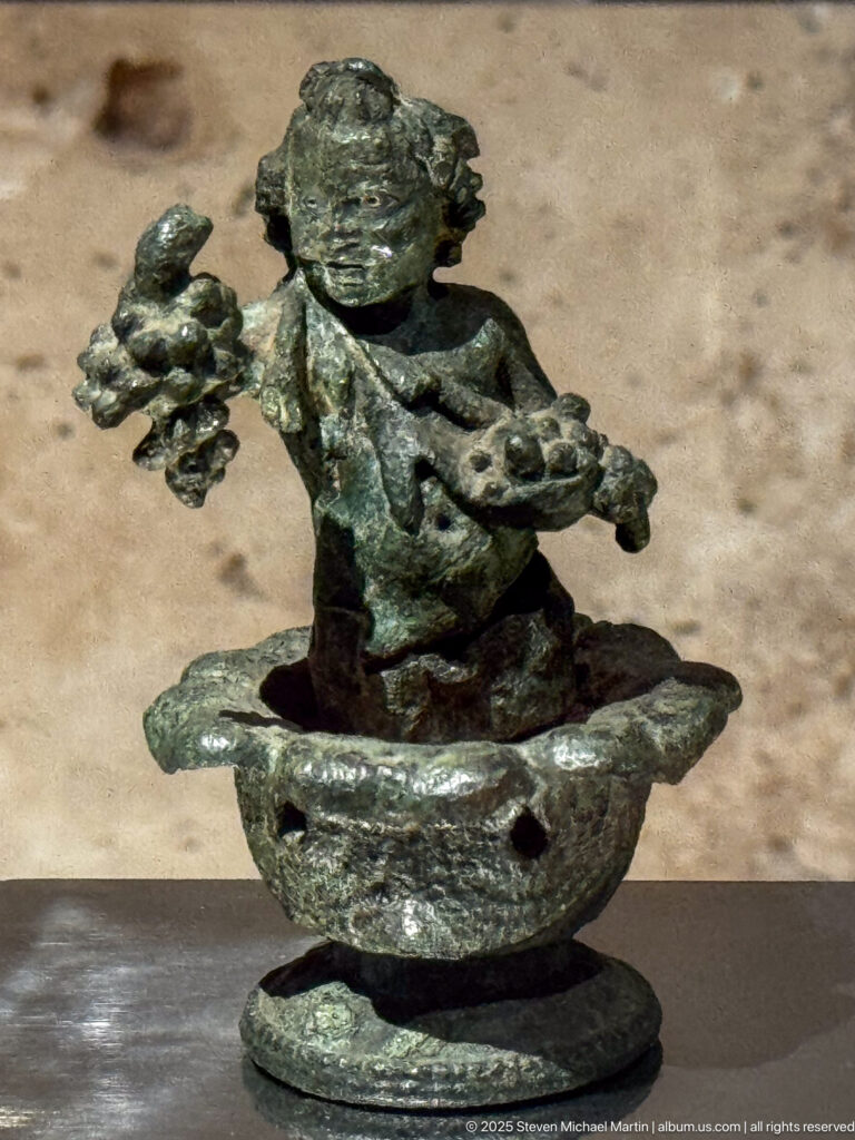 Small patinated bronze figure with outstretched arms seated over a shallow elongated base on a circular mount.