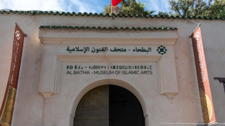 Close view of Al Batha Museum entrance inscription above a horseshoe arch, with green roof tiles and pale carved surround.
