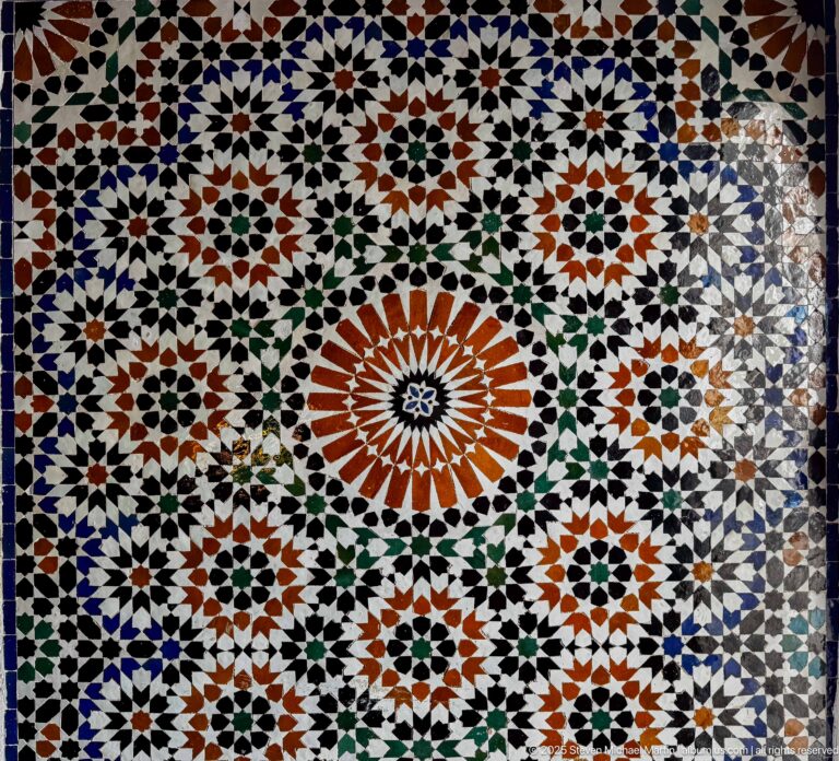 Multicolored zellij panel with large orange-and-white central starburst surrounded by interlocking stars, polygons, and rosettes.
