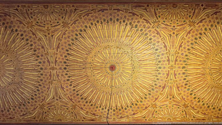 Ornate painted ceiling with three large golden starburst rosettes surrounded by dense geometric and floral motifs.