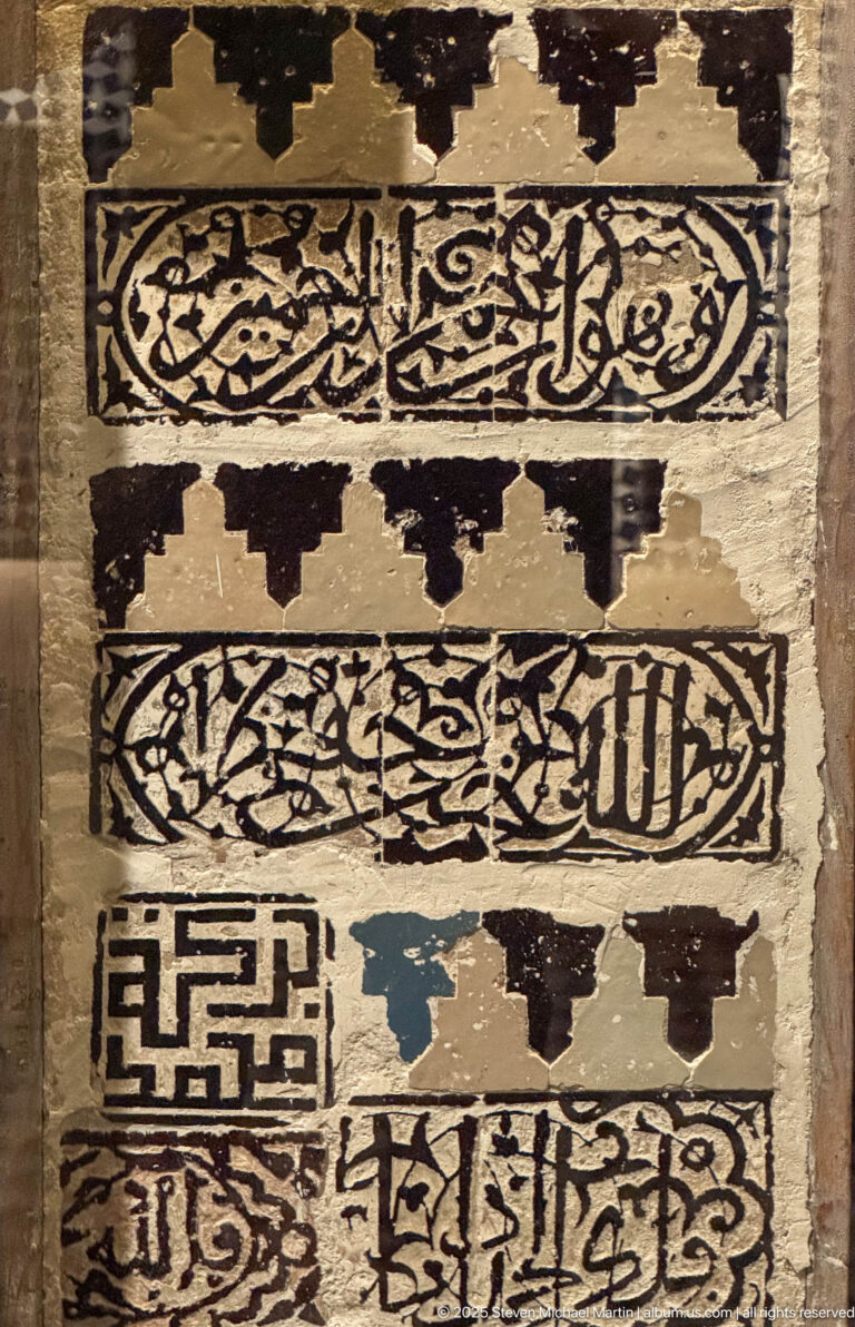 Weathered panel fragment with horizontal Arabic calligraphy bands, including cursive script and a square geometric inscription.