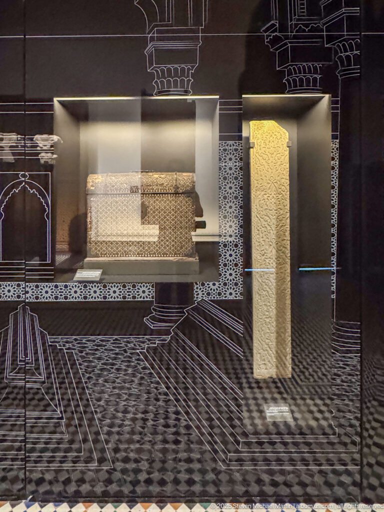 Display case with a broad horizontal carved architectural fragment beside a tall narrow decorated panel.