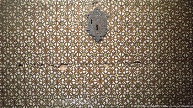 Close view of an inlaid wooden surface covered with small repeating rosettes around a vertical metal lock plate.