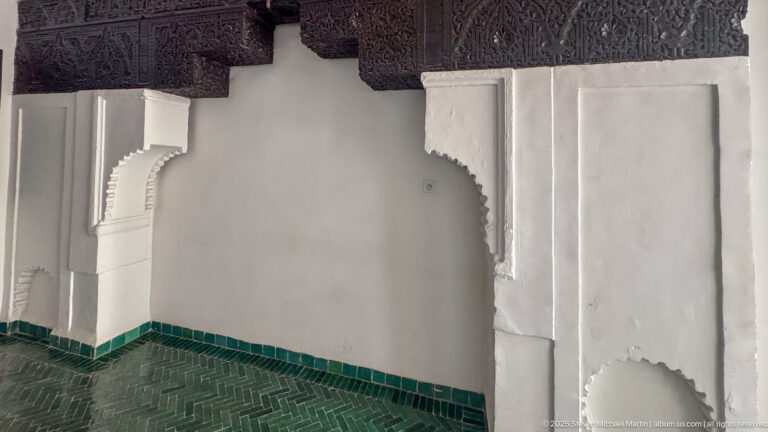 White interior corner with carved plaster arch, ornate dark lintel, green tile base, and patterned dark floor.