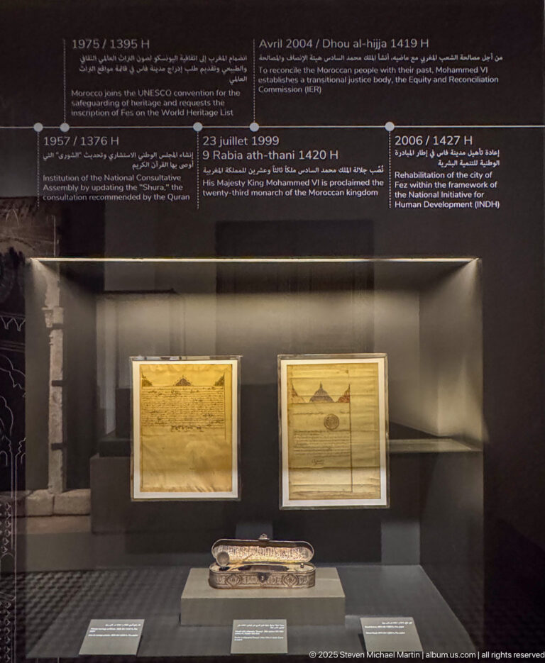 Two framed historical documents above a long narrow ceremonial object in a museum case.