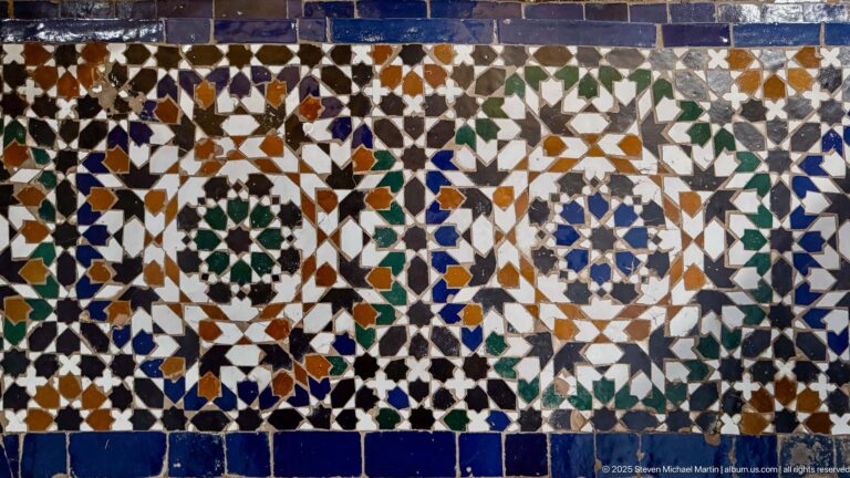 Rectangular multicolored zellij panel with repeated stars, circular rosettes, interlocking polygons, and dark blue border tiles.