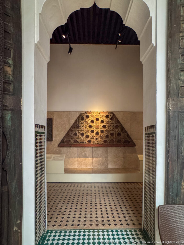 Large semicircular carved or pierced architectural panel mounted on a wall beyond an arched, tiled museum interior.