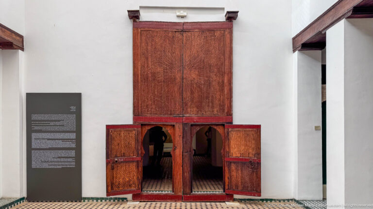 Tall carved wooden door with richly ornamented upper panels and four smaller lower leaves opened around two passage openings.
