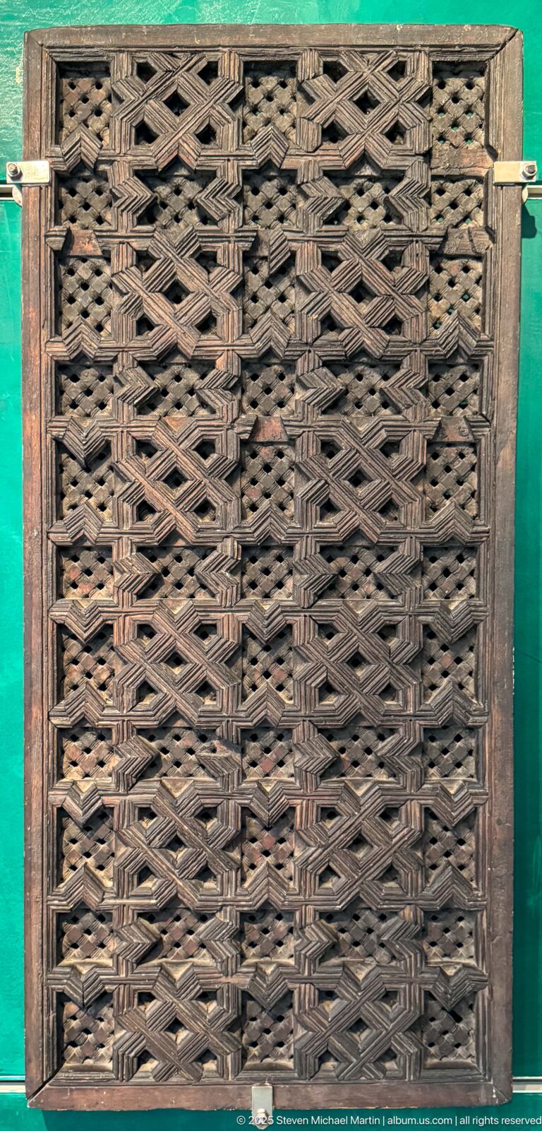 Rectangular dark wooden lattice screen with interlocking strips forming repeated stars, diamonds, and angular geometric openings.