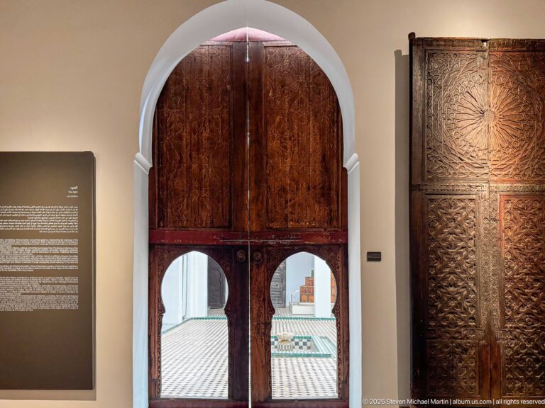 Carved wooden doors with two arched lower openings beside a tall panel centered on a radiating carved rosette.