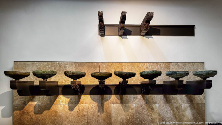 Eight bronze sounding bowls from the 1357 Dar al-Magana hydraulic clock in Fes, displayed below carved wooden supports.