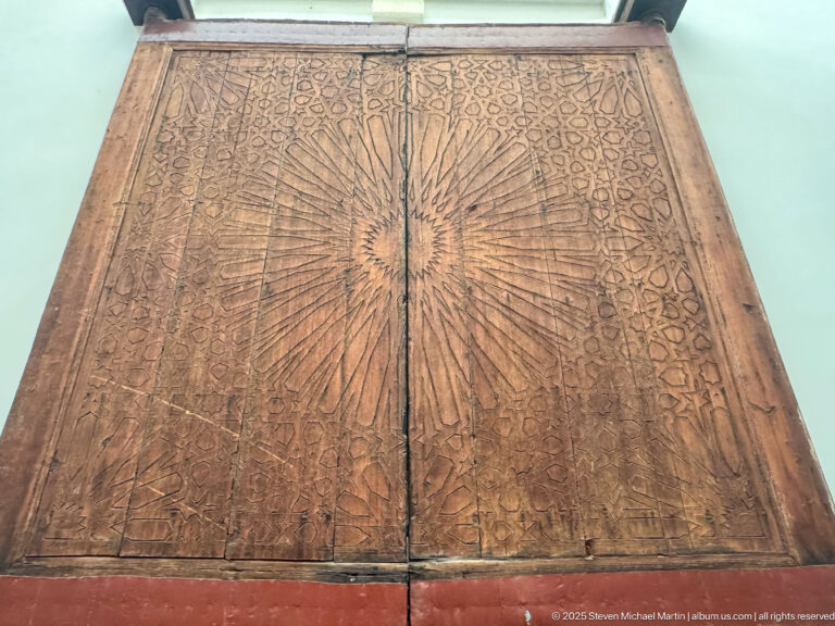 Close-up of paired carved wooden panels with a central radiating sunburst rosette and dense surrounding geometric ornament.