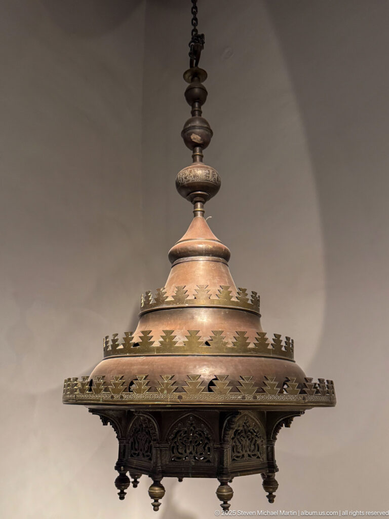 Tiered metal hanging lamp with pierced circular canopy, scalloped ornament, small hanging finials, and stacked central suspension pieces.