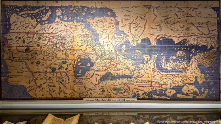 Large historic-style map with tan land, deep blue seas, red lines, many place labels, symbols, and worn painted areas.