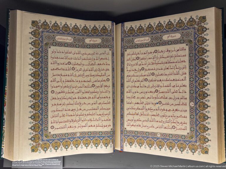 Open Arabic manuscript with neat text, red marks, and elaborate blue, gold, green, and floral illuminated borders.