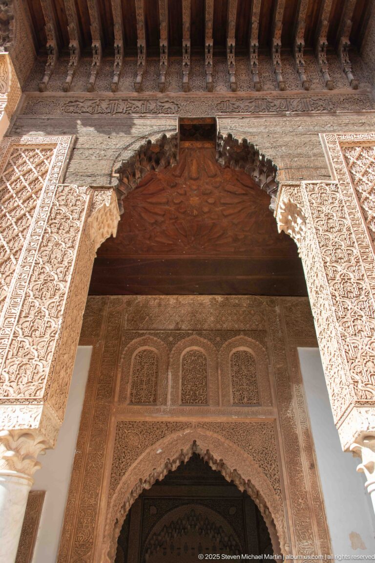 Ornate stucco-framed entrance with slender columns, scalloped arch, timber canopy, and a second pointed arch inside.