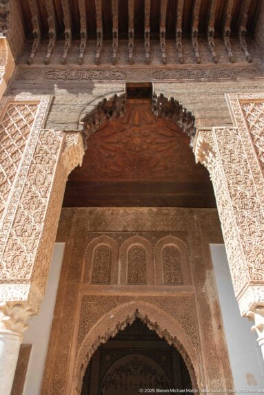 Ornate stucco-framed entrance with slender columns, scalloped arch, timber canopy, and a second pointed arch inside.