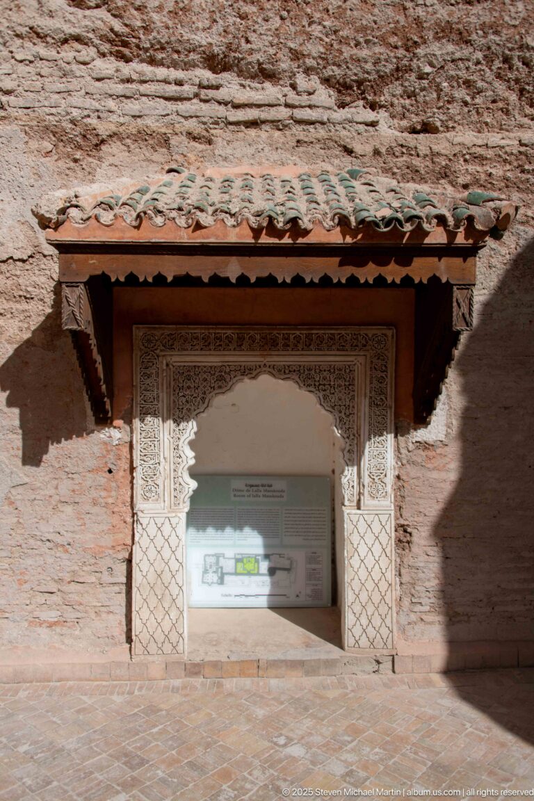 Site-plan display inside a carved rectangular opening beneath a small green-tiled canopy in an earthen wall.