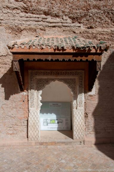 Site-plan display inside a carved rectangular opening beneath a small green-tiled canopy in an earthen wall.