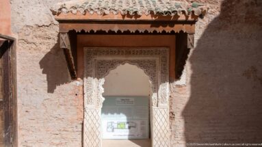 Carved wall niche with a site plan for the Room of Lalla Massouda beneath a shallow green-tiled canopy.