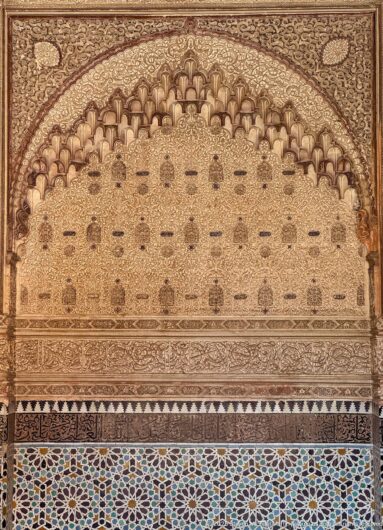 Carved stucco horseshoe arch with dense relief ornament above multicolored geometric zellij in the Room of Lalla Massouda.