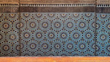 Frontal wall of multicolored zellij with repeating star rosettes beneath narrow carved and patterned decorative bands.