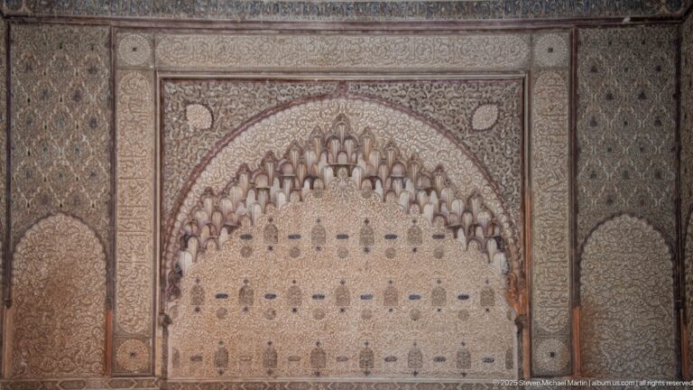 Symmetrical carved stucco arch edged with clustered muqarnas forms and surrounded by dense relief panels.