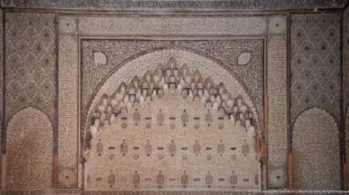 Symmetrical carved stucco arch edged with clustered muqarnas forms and surrounded by dense relief panels.