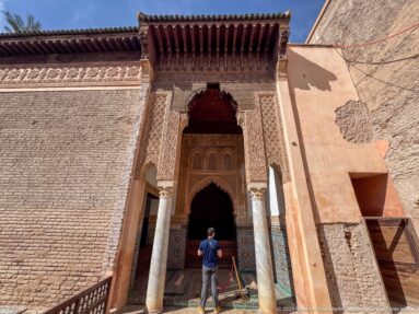 Visitor approaching an ornate carved portal with columns and timber eave in the courtyard of the Saadian Tombs.